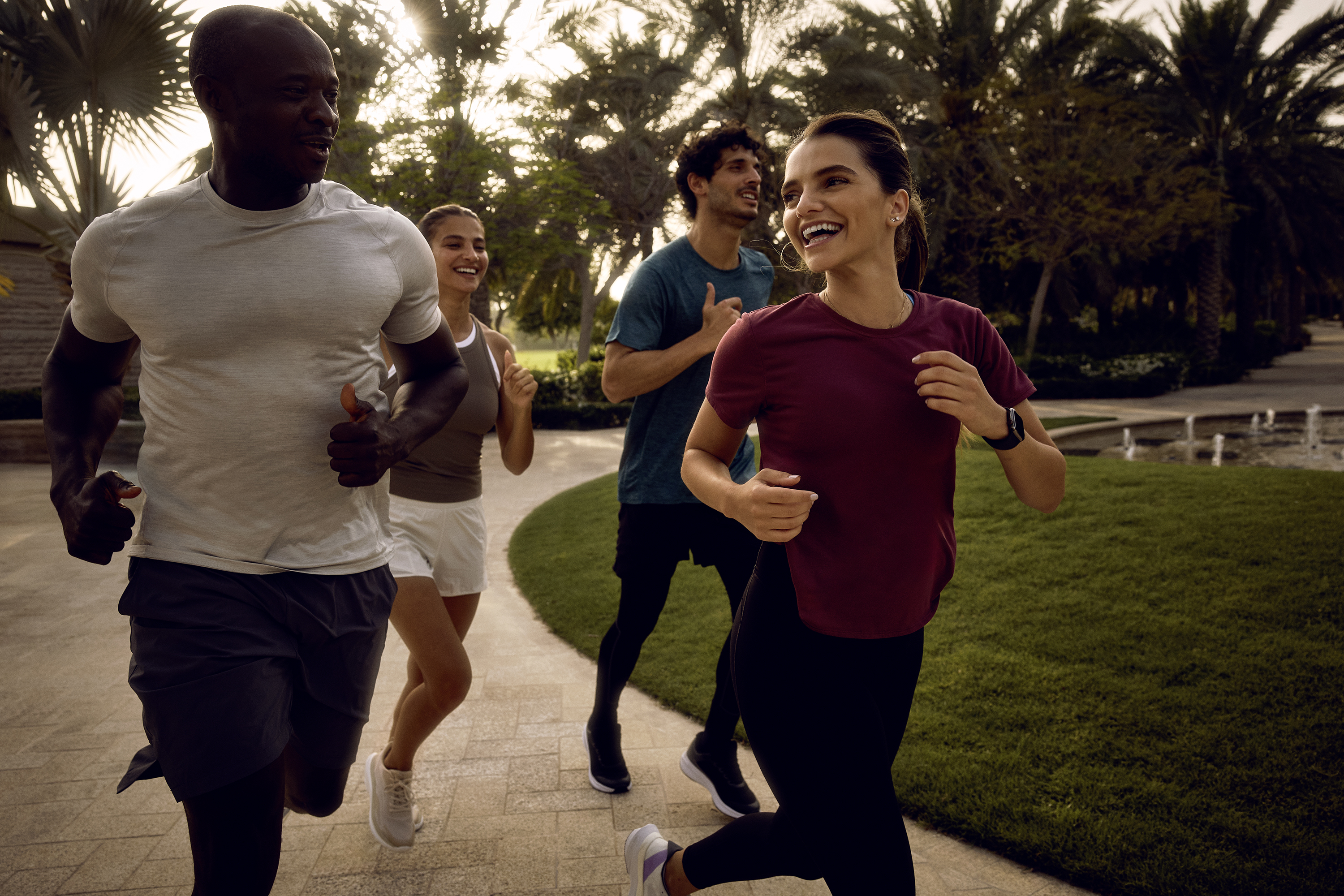 Four people jog a curved path beside a lawn and a fountain.